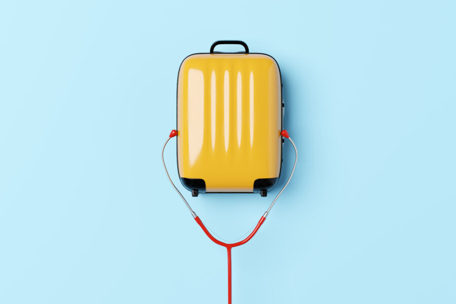 Conceptual image of a yellow suitcase with a stethoscopes earpiece around it with a blue background to illustrate ideas around travel and health insurance