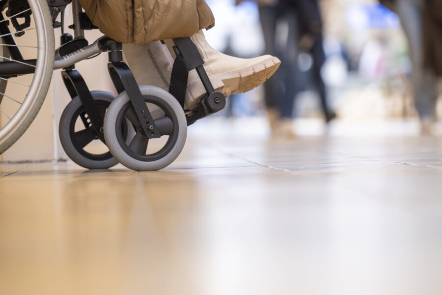 Close-up of a person in a wheelchair at a public facility with passersby in the background